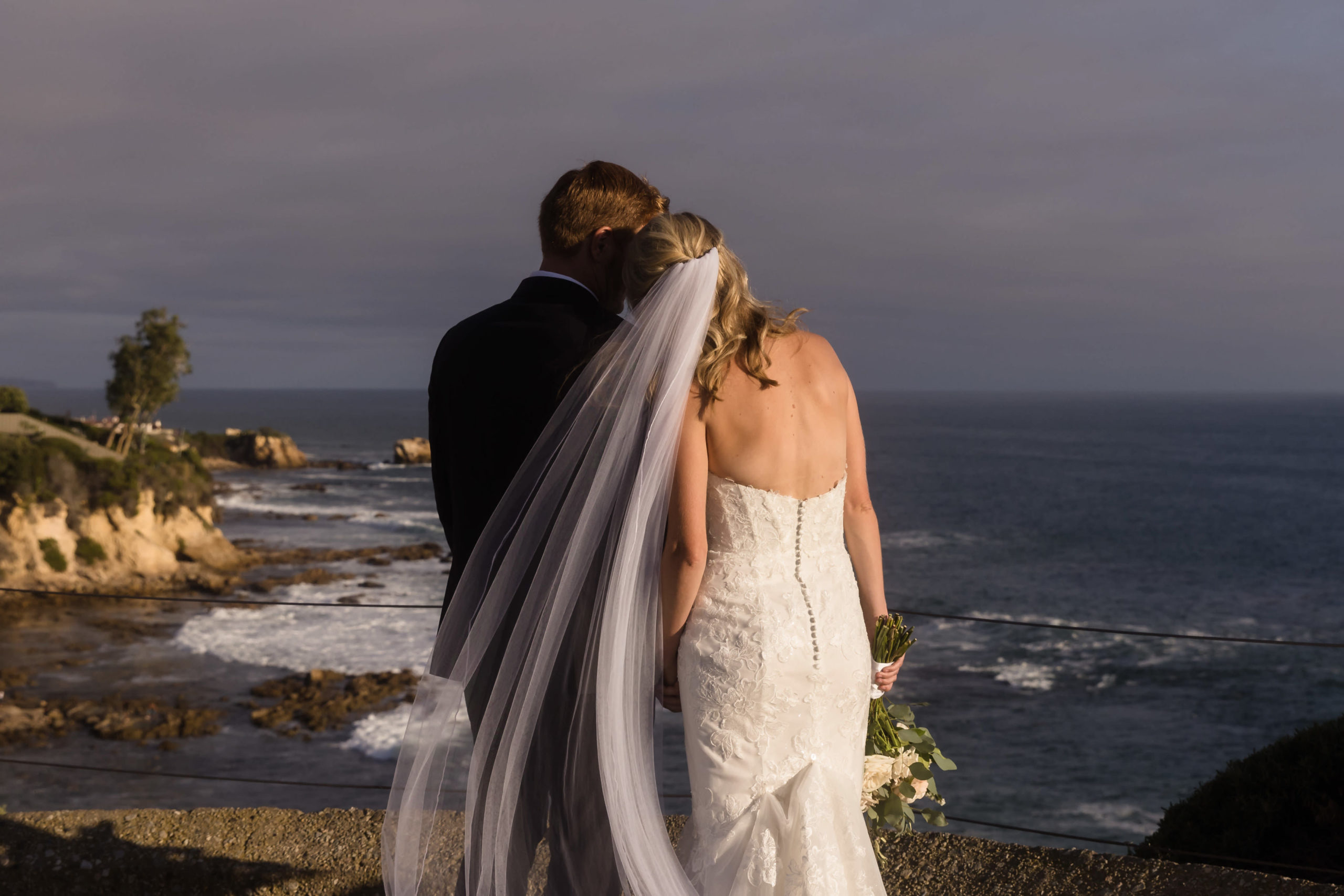 Newlywed couple sharing an embrace with each other with their backs to the camera and looking over beach view, captured by Christopher Brown Weddings