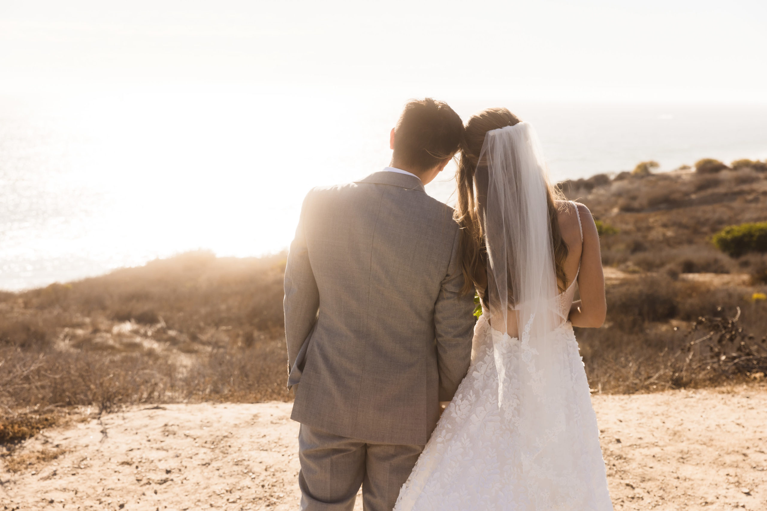 Bride and groom posing in front of beach view during golden hour, taken by Joshua Tree wedding photographer Christopher Brown