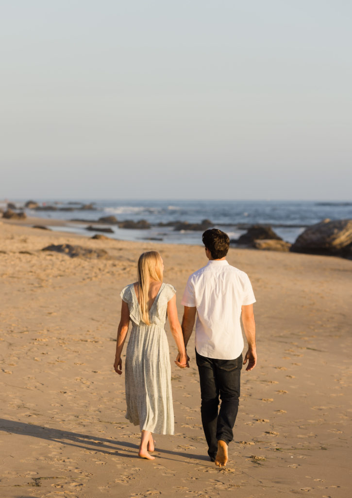 Engaged couple walking together with their backs to the camera at Crystal Cove, one of the top 6 Laguna Beach engagement photo locations
