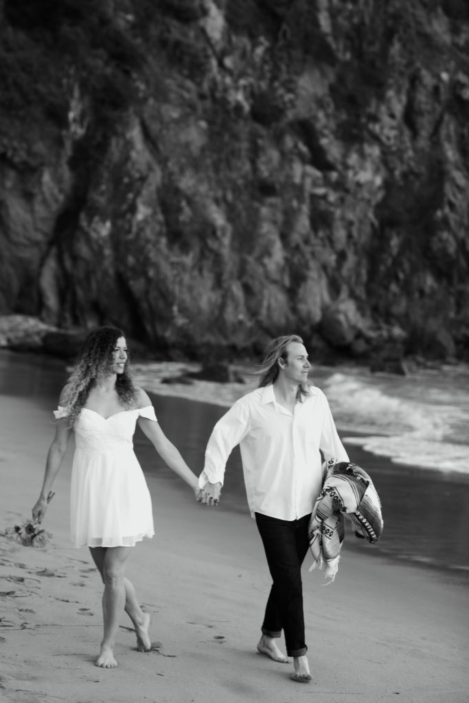 Black and white photo of couple holding hands while walking along the beach at Treasure Island, one of the top 6 Laguna Beach engagement photo locations