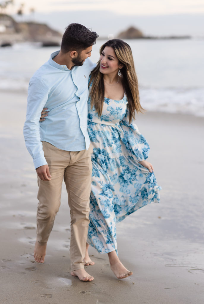 Couple smiling at each other as they walk along the beach for their engagement session with Christopher Brown