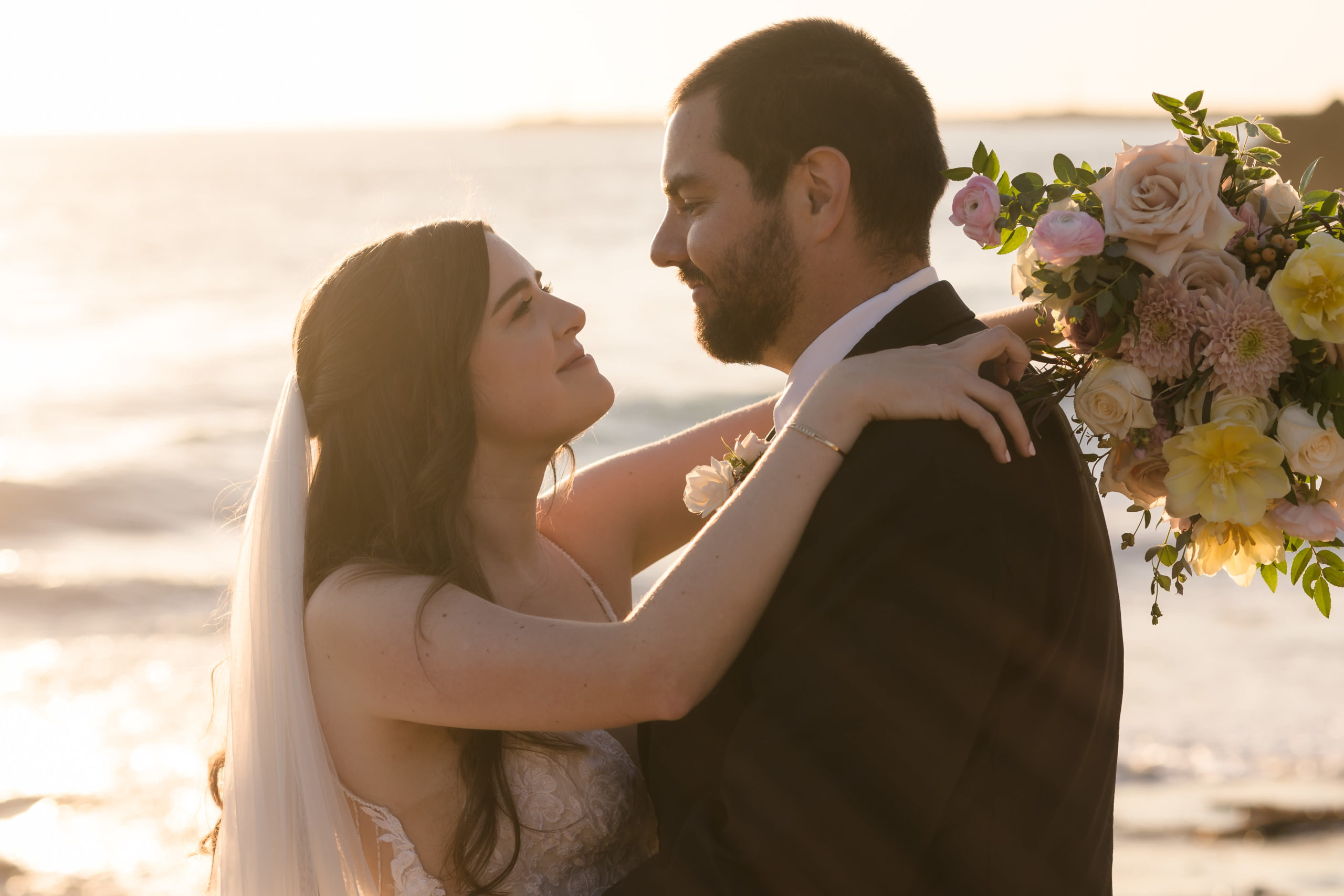 The Top 8 Beach Wedding Venues In Orange County, CA. Newlywed couple sharing an embrace on the beach during golden hour.