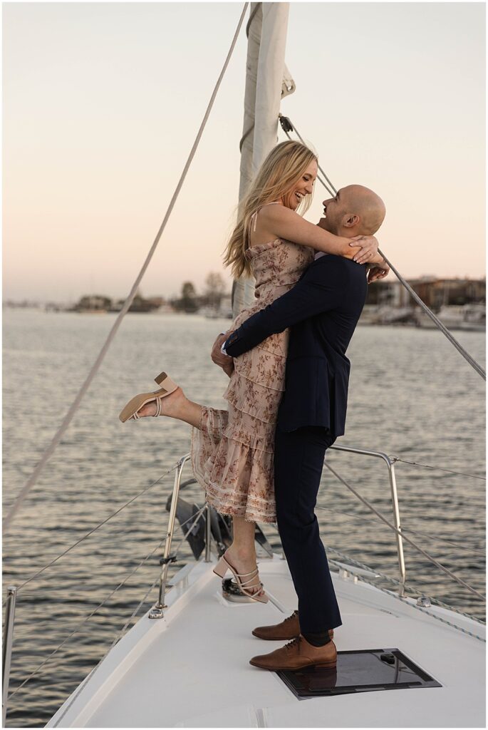 Man in black suit lifting woman in air on a boat at Newport Beach harbor