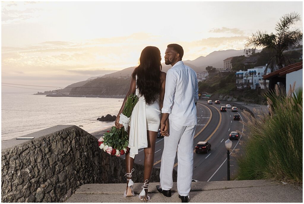 Couple looking down on the Pacific Coast Highway in Malibu overlooking the coast for Malibu engagement session