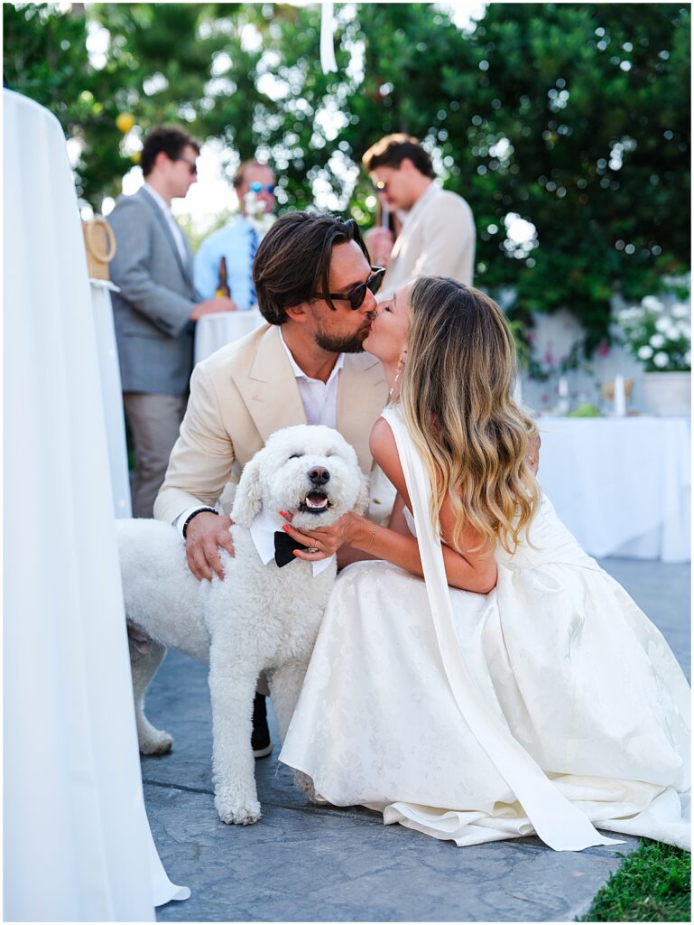 Bride and groom kissing in front of dog wearing a bowtie