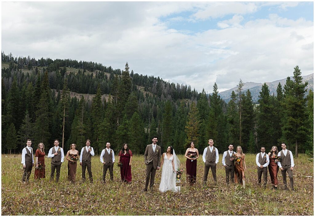 Bride and groom standing with their bridal party in open field with mountains behind in Idaho