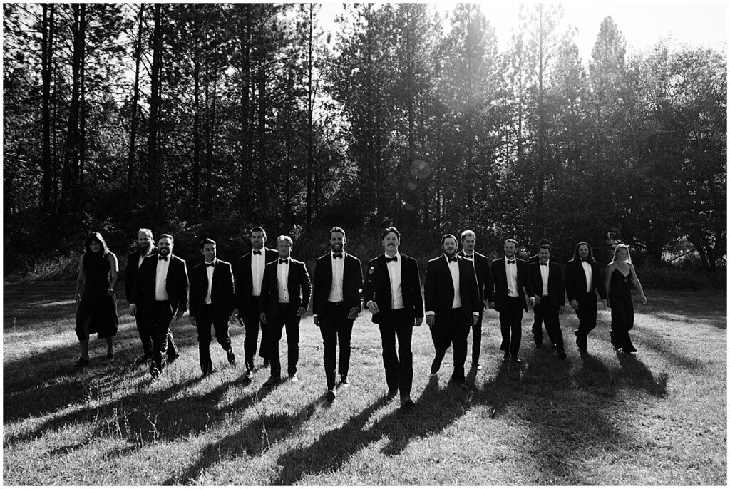 Groom walking across a field with groomsmen all wearing black tuxedos