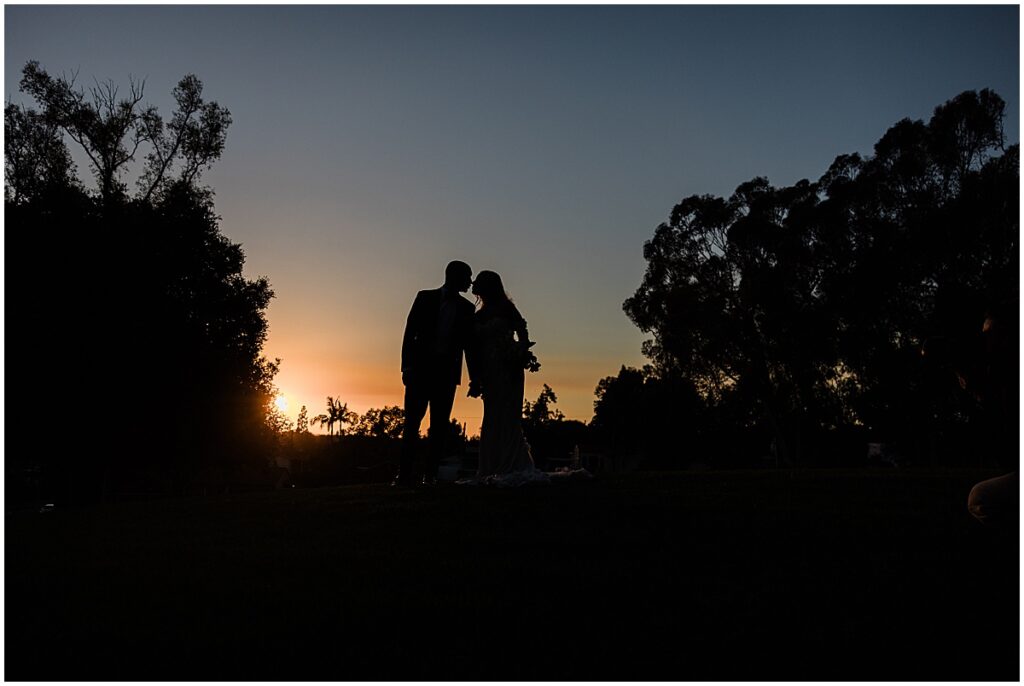 Bride and groom kissing against sun setting sky