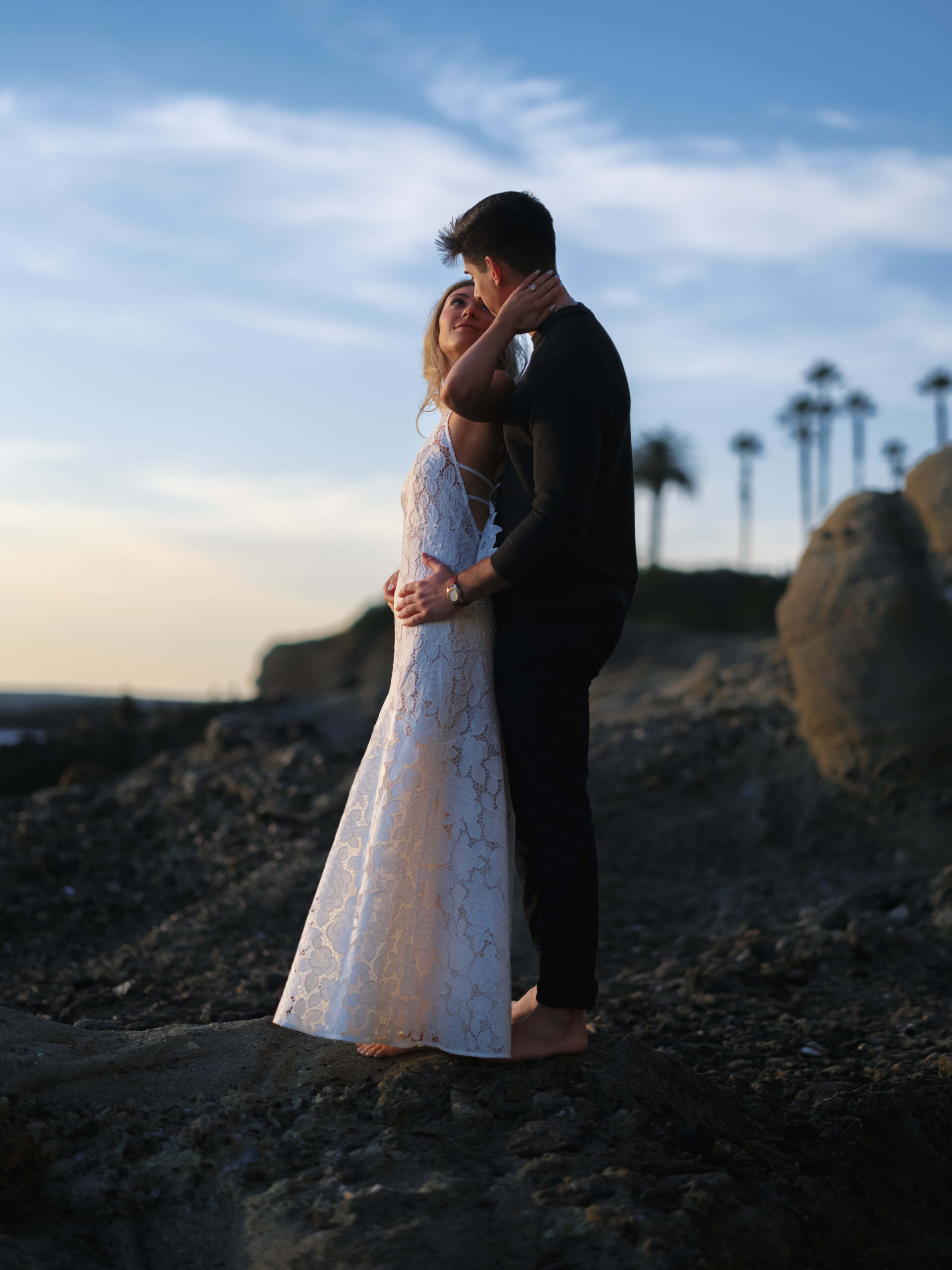 Man standing behind woman and her reaching round to look at him at Treasure Island, Laguna Beach