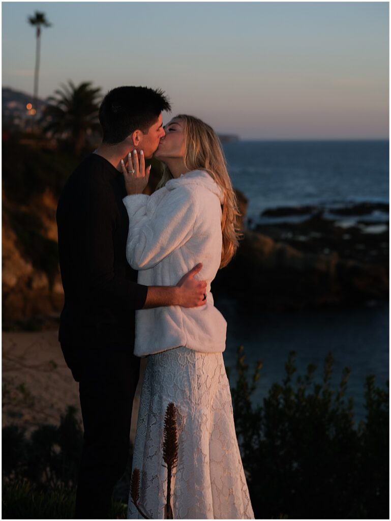 Couple in black and white outfits kissing on Laguna beach for engagement photos