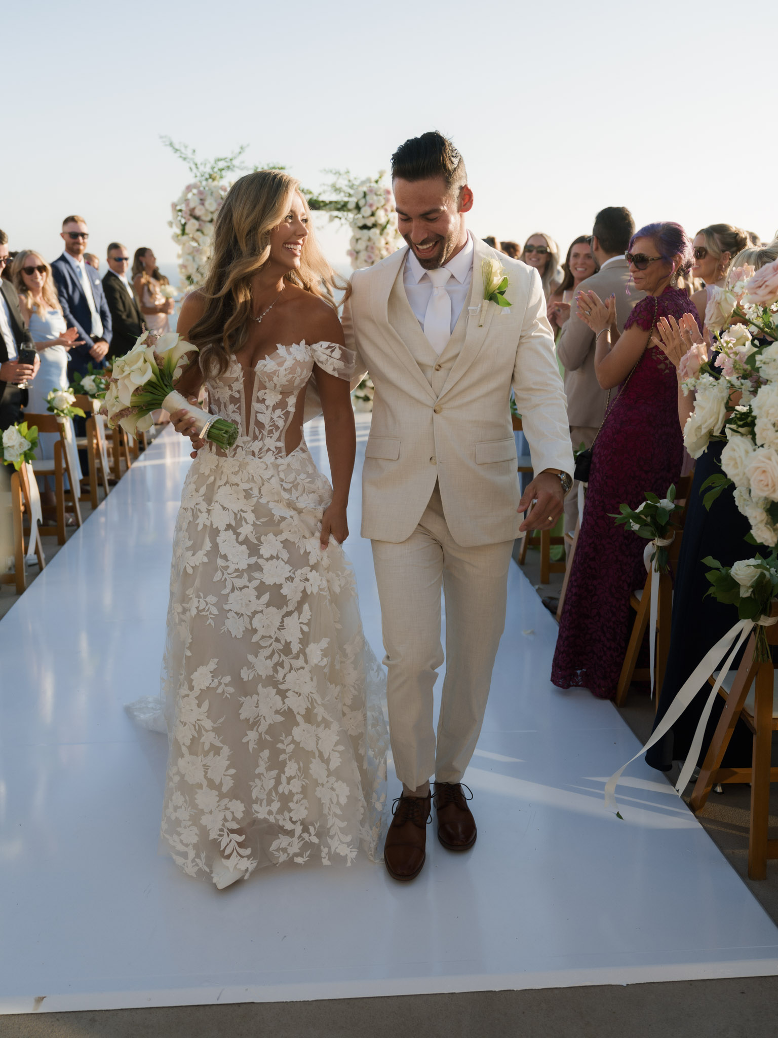 Laughing newlyweds walking hand in hand down the aisle as wedding guests clap during the recessional at Surf & Sand Resort.