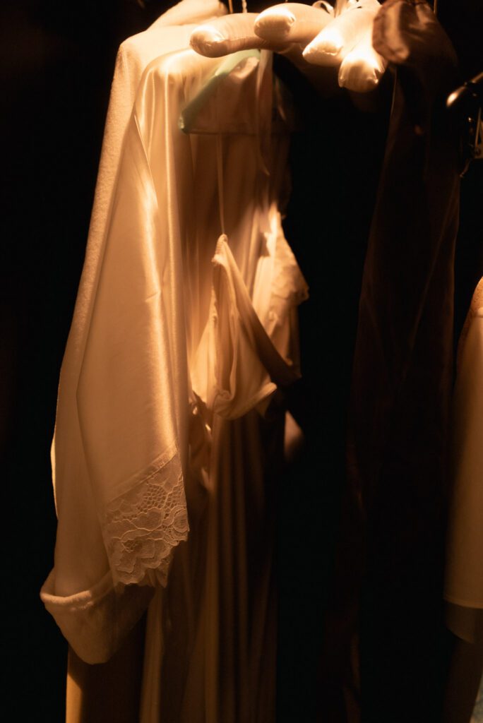Silk bridal robe with delicate lace sleeve cuffs hanging on a padded hanger in soft warm closet light.