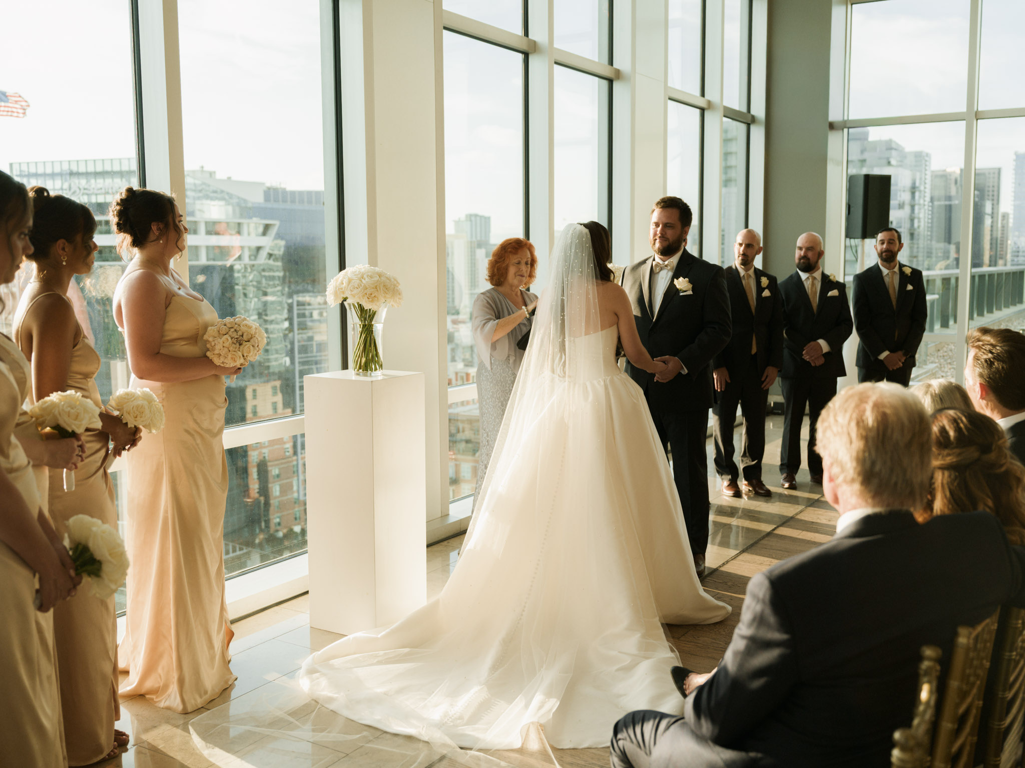 Bridesmaids in champagne satin gowns and groomsmen in black suits flanking the bride and groom at the altar in warm afternoon light .