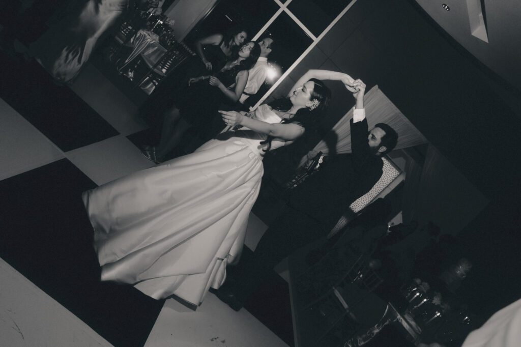 Black and white capture of the groom spinning the bride during late-night open dancing surrounded by celebrating wedding guests.