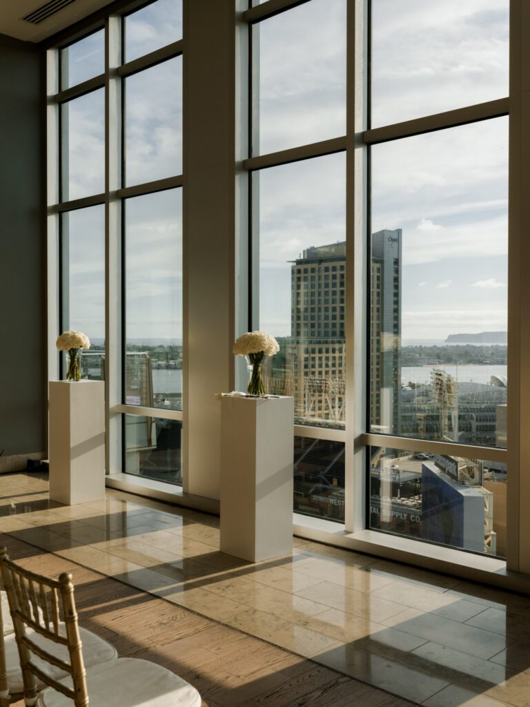 Two minimalist white pillar pedestals topped with round white floral arrangements framing views of Petco Park and San Diego Bay .